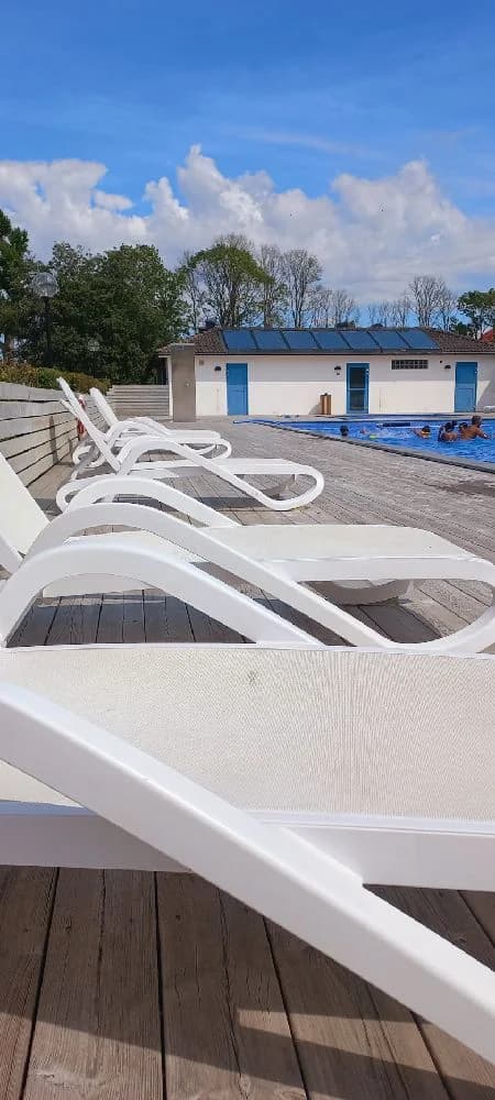 En utomhusmiljö vid Allégården Kastlösa med utemöbler av kompositmaterial i skuggan bredvid en swimmingpool.