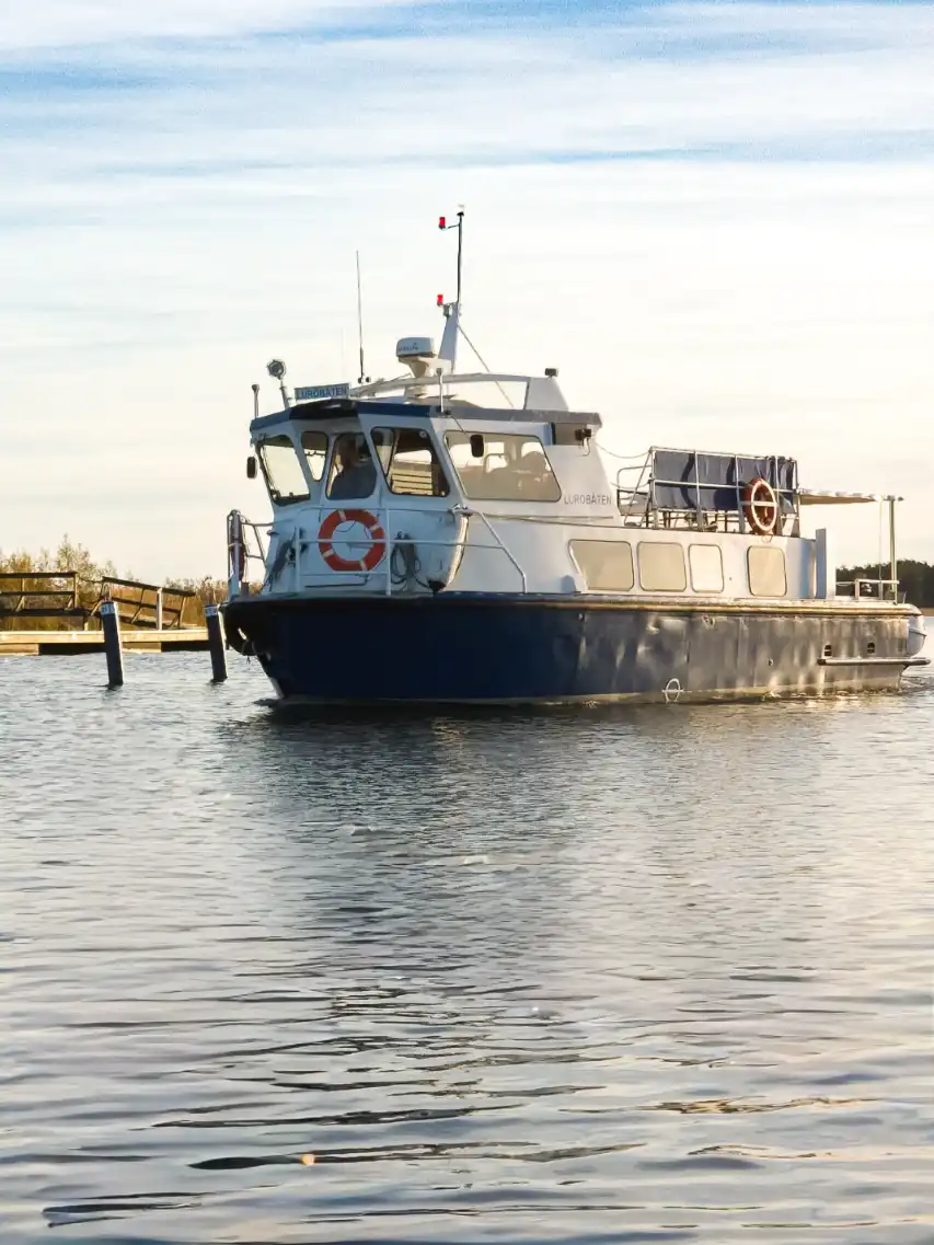 En vy över Ekenäs gästhamn & camping, med flera båtar och vattenfarkoster förtöjda vid bryggan i den lugna vattenleden.