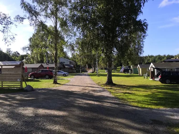 En bild av Överhörnäs Camping med en uppfart som leder till en grupp stugor. Grönt gräs och en välskött trädgård omger området, med parkering tillgänglig för besökare.