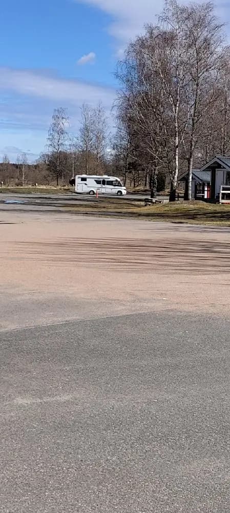 En asfalterad väg leder in till Stenrösets camping i Trollhättan, med parkerade fordon synliga vid vägkanten och omgivningar som antyder en öppen campingplats.