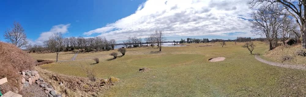 En vidsträckt grässlätt under en molnig himmel vid Stenrösets Camping i Trollhättan.
