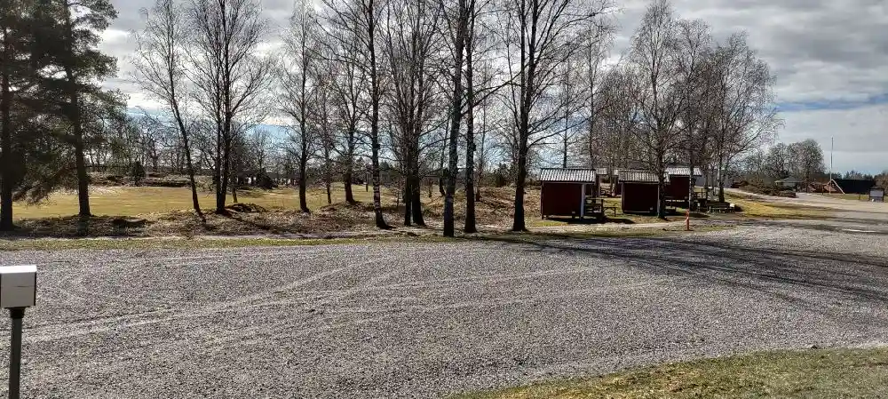 En asfalterad väg leder in till Stenrösets Camping i Trollhättan, omgiven av grönskande träd och öppna landskap i en lantlig miljö.