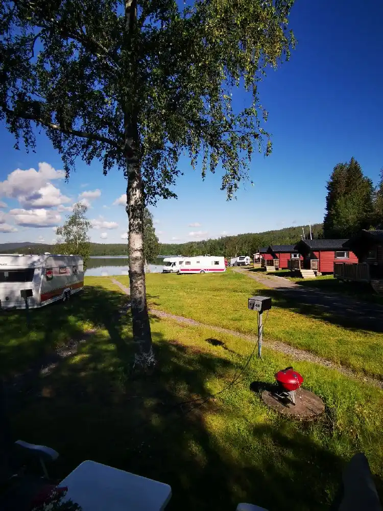 Bild av Snibbens Camping med en grön gräsyta där flera husbilar och tält står uppställda. Området är omgivet av ett öppet landskap, vilket skapar en avkopplande campingmiljö.