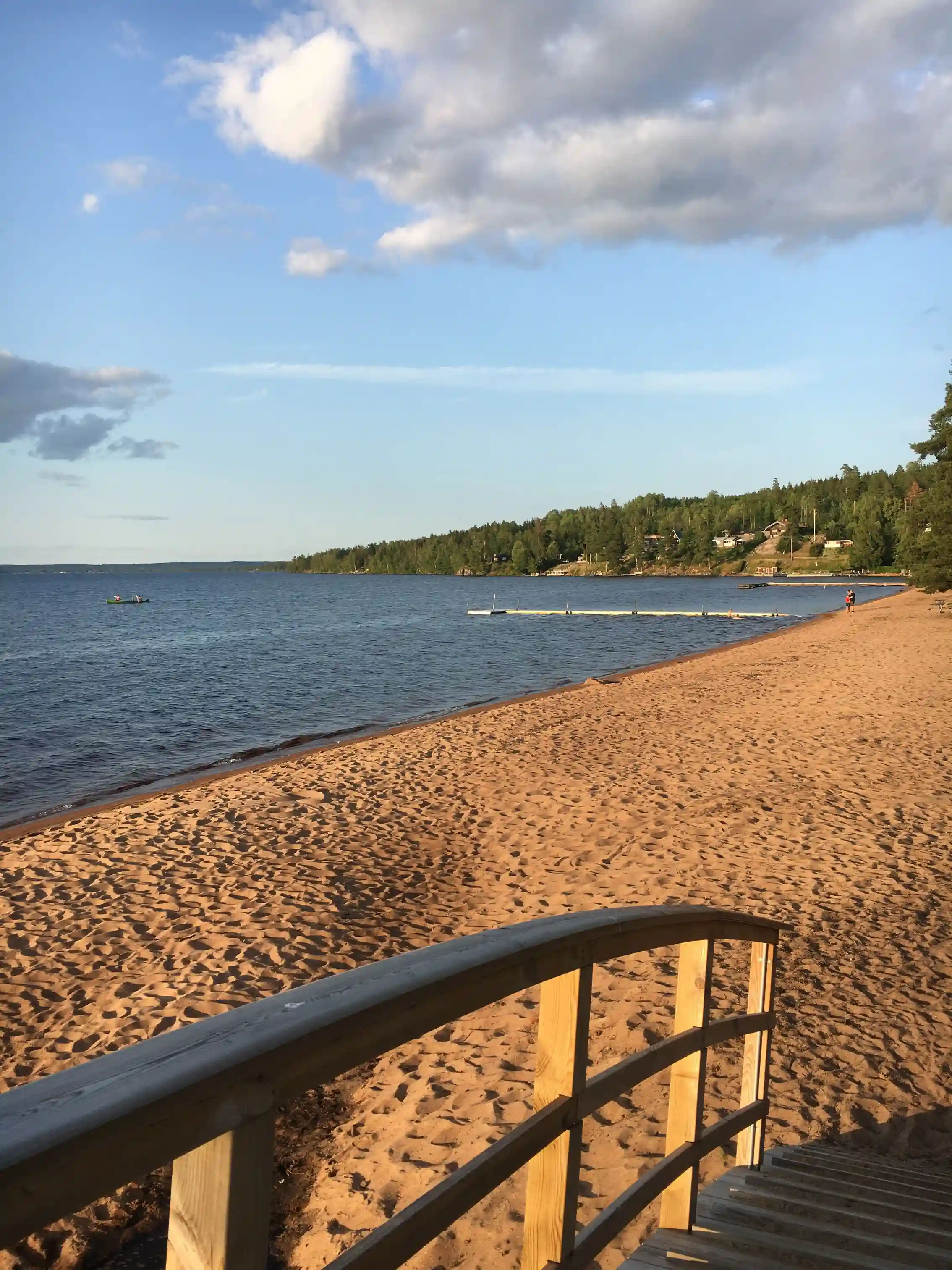 En solig dag vid Otterbergets bad och camping, med en vidsträckt blå himmel och ett glittrande vattendrag som sträcker sig mot horisonten, kantad av en sandstrand och kustlinje.
