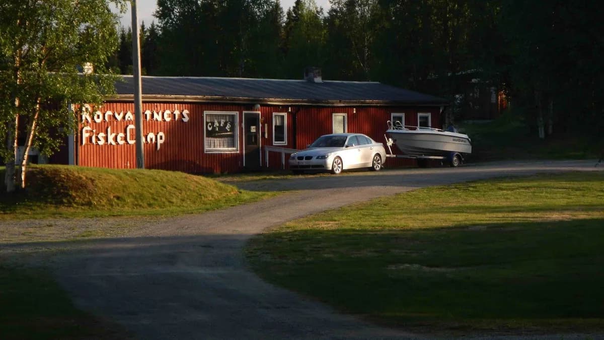 En sportbil står parkerad på en grusplan vid Rörvattnets fiskecamp, omgiven av grönskande natur.