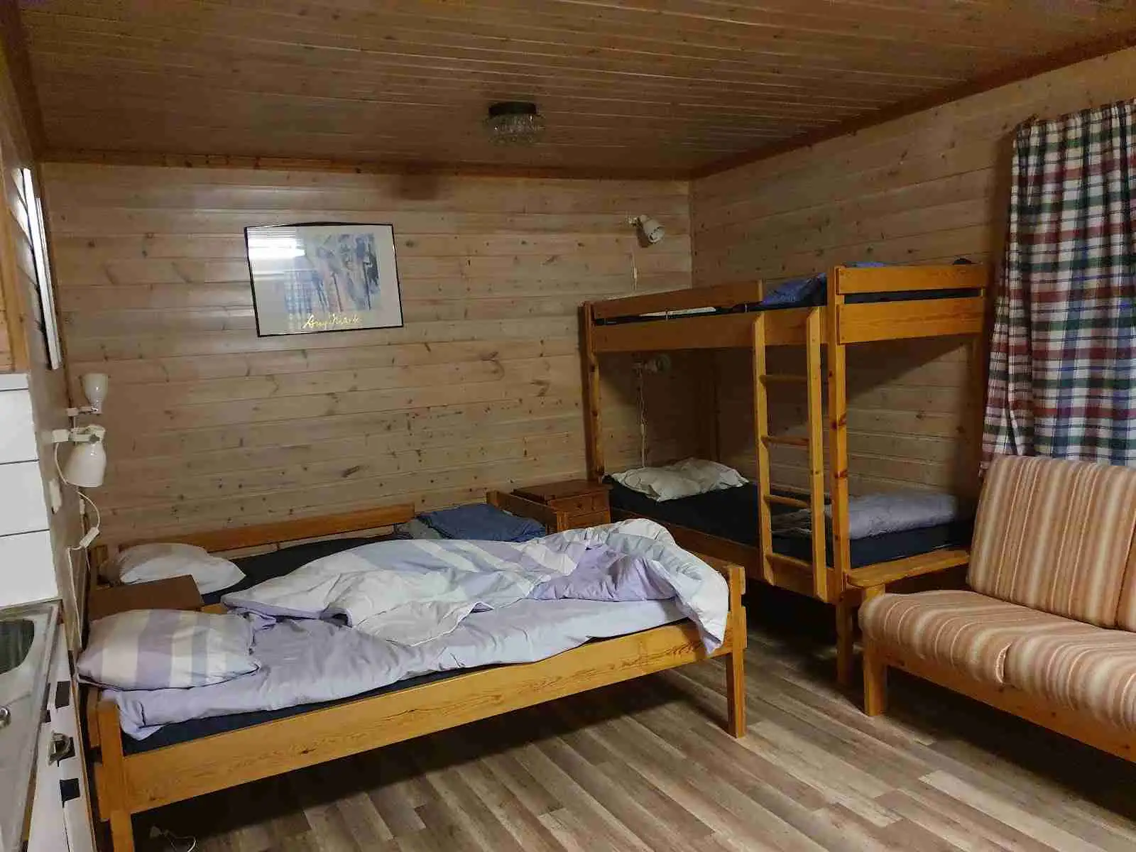 En campingstuga med trägolv och en inredning av ljusa trämöbler, inklusive en våningssäng. Enkel och funktionell design för bekväm övernattning.
