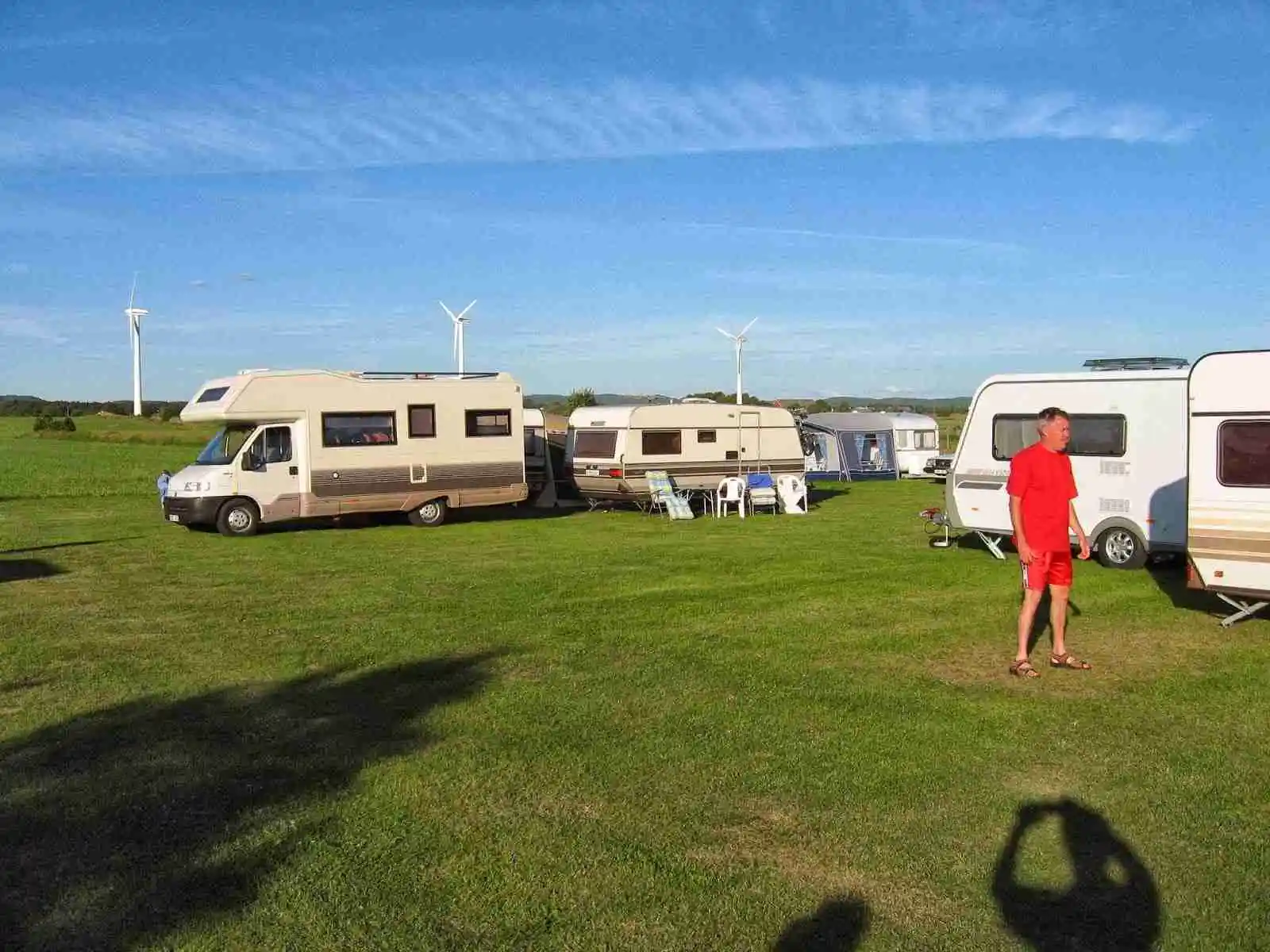 En husbil står parkerad på en campingplats under en molnig himmel, med ett tält och andra campingtillbehör i närheten, på Rödlix Hostel & Camping.