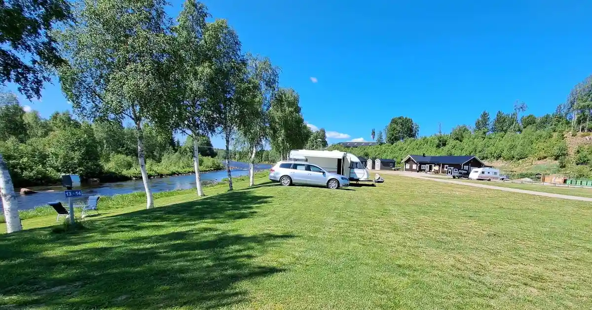 En husbil är parkerad på en grön campingplats med skog i bakgrunden vid Lillhärdals camping.