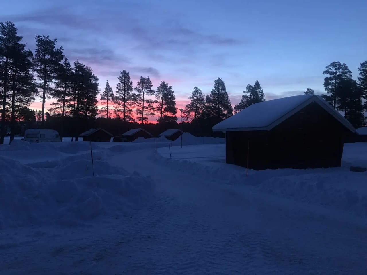 En vinterbild vid Camp Viking, visar en snötäckt stuga i skymningen med en fridfull och kylig landskapsvy.