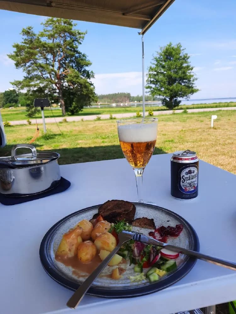 Ett dukat bord utomhus med olika maträtter och drycker, med tallrikar, glas och bestick, på Skeppeviks camping.