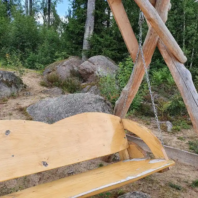 En träbänk placerad i en park, omgiven av naturliga material som träplankor och solstolar, under en klar himmel på Abrahams Camp.