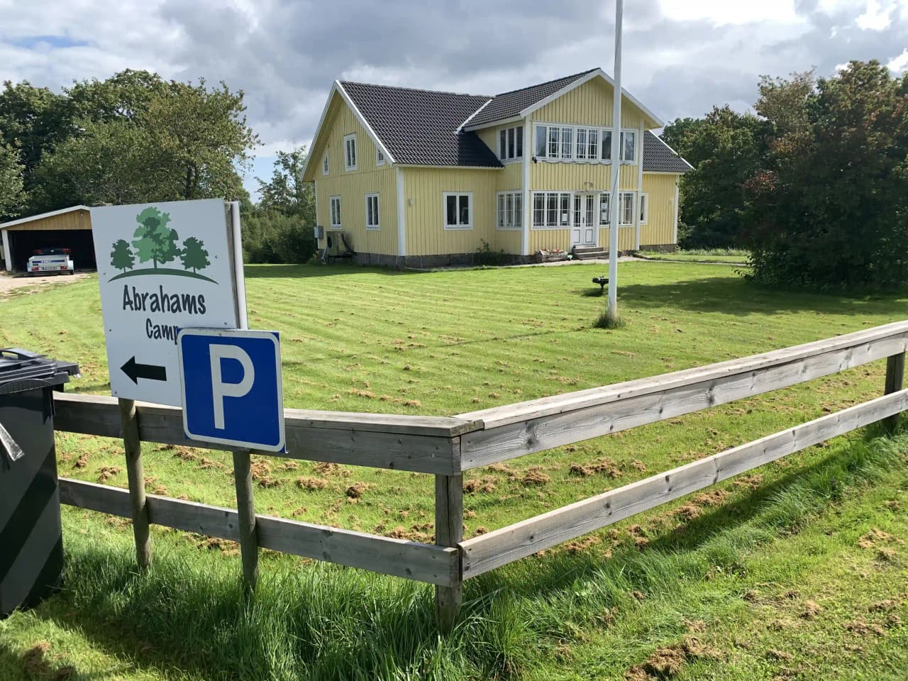 En grön gräsmatta med ett staket av träplankor omger ett hus, med en uppfart i bakgrunden på Abrahams Camp.