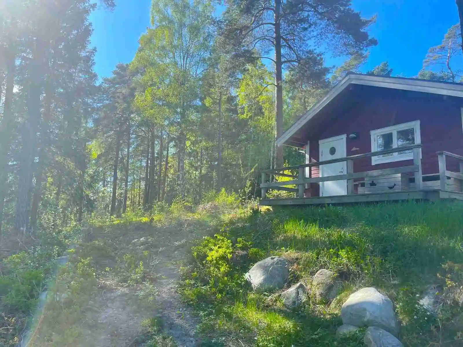 En trästuga omgiven av skog på Waxholms camping, belägen i ett lantligt område med sluttande terräng.