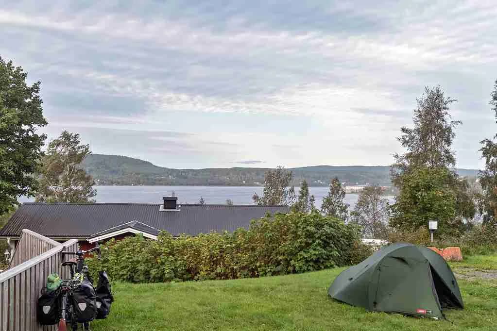 En campingplats på Solbacken med grönt gräs och uppfällda tält under en molnig himmel. En mindre bil är parkerad i närheten.