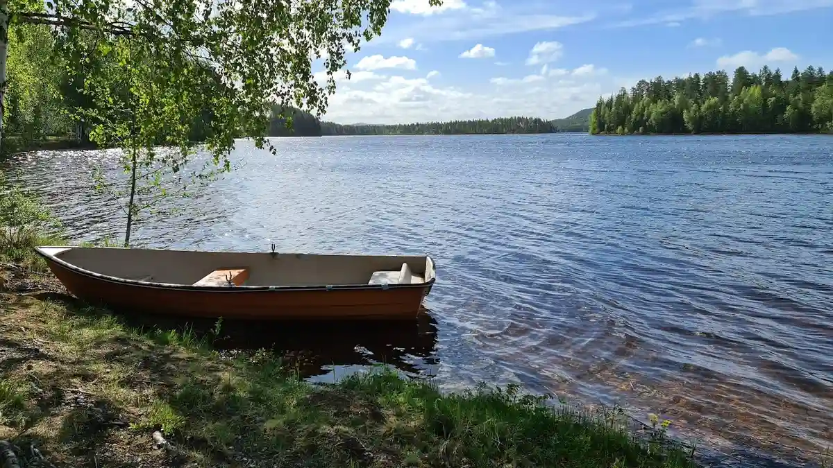 En liten båt flyter på ett lugnt vattendrag omgivet av grönskande natur vid Lapplandsportens camping.