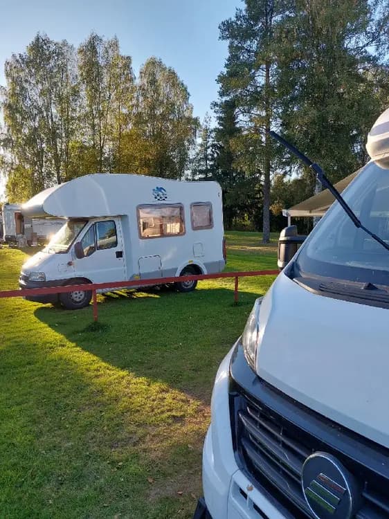 En campingplats vid Grebbestadfjorden med flera husbilar och husvagnar uppställda. I bakgrunden syns grönska och träd, vilket skapar en naturnära miljö.