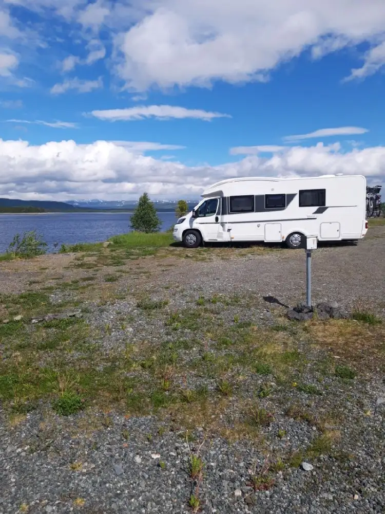En husbil parkerad vid Kallsedet Camping med gröna omgivningar i bakgrunden, redo för en roadtrip.