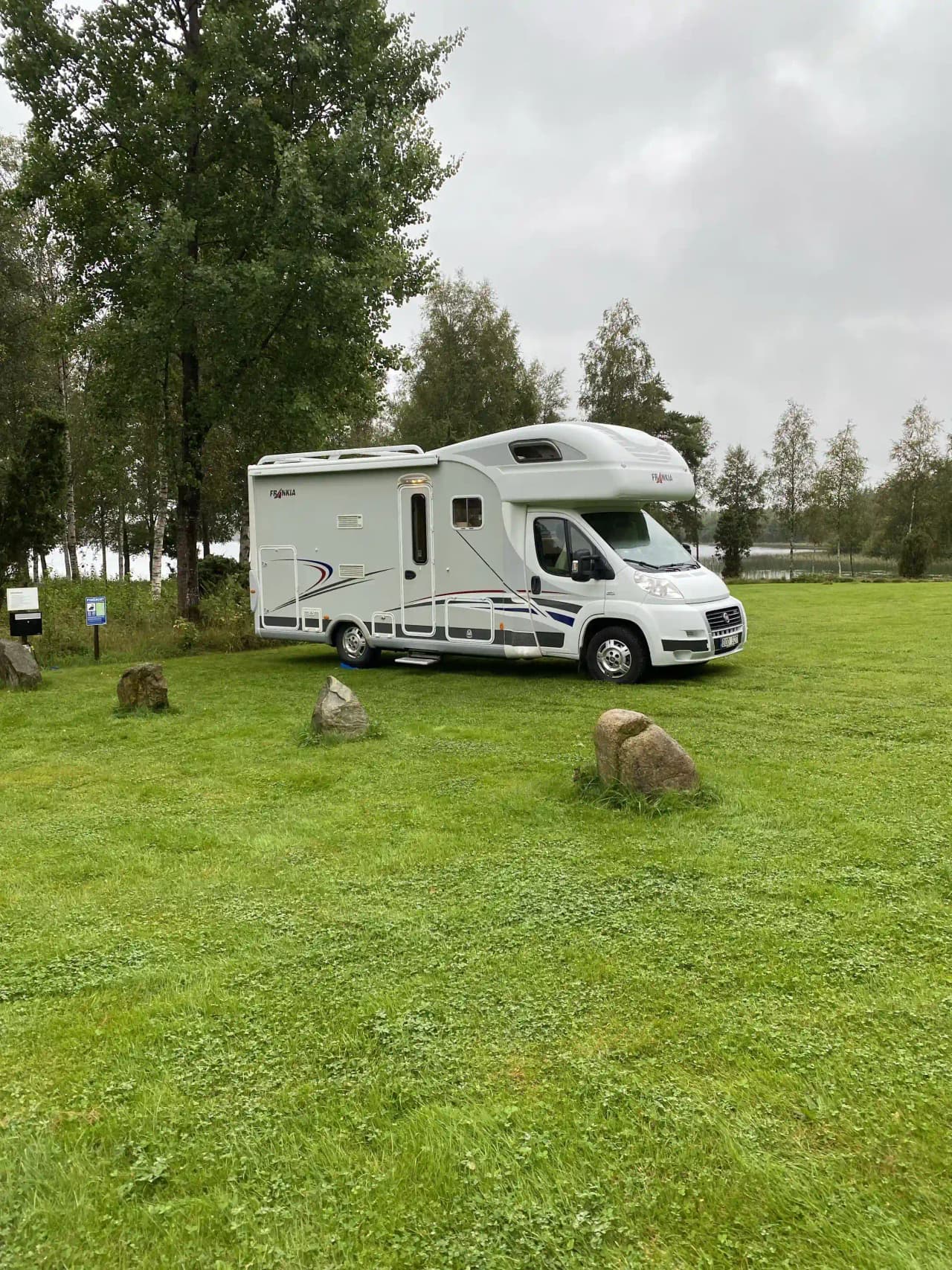 En husvagn och skåpbil står parkerade på en grön gräsmatta framför Moarps B&B, omgivna av en lummig parkmiljö.