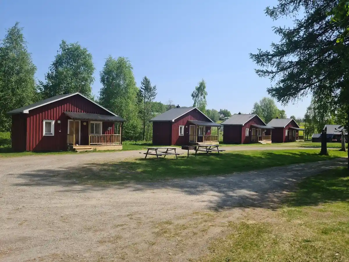 En grön campingplats med stugor omgivna av träd och gräsmattor i ett lantligt område i Norråker.