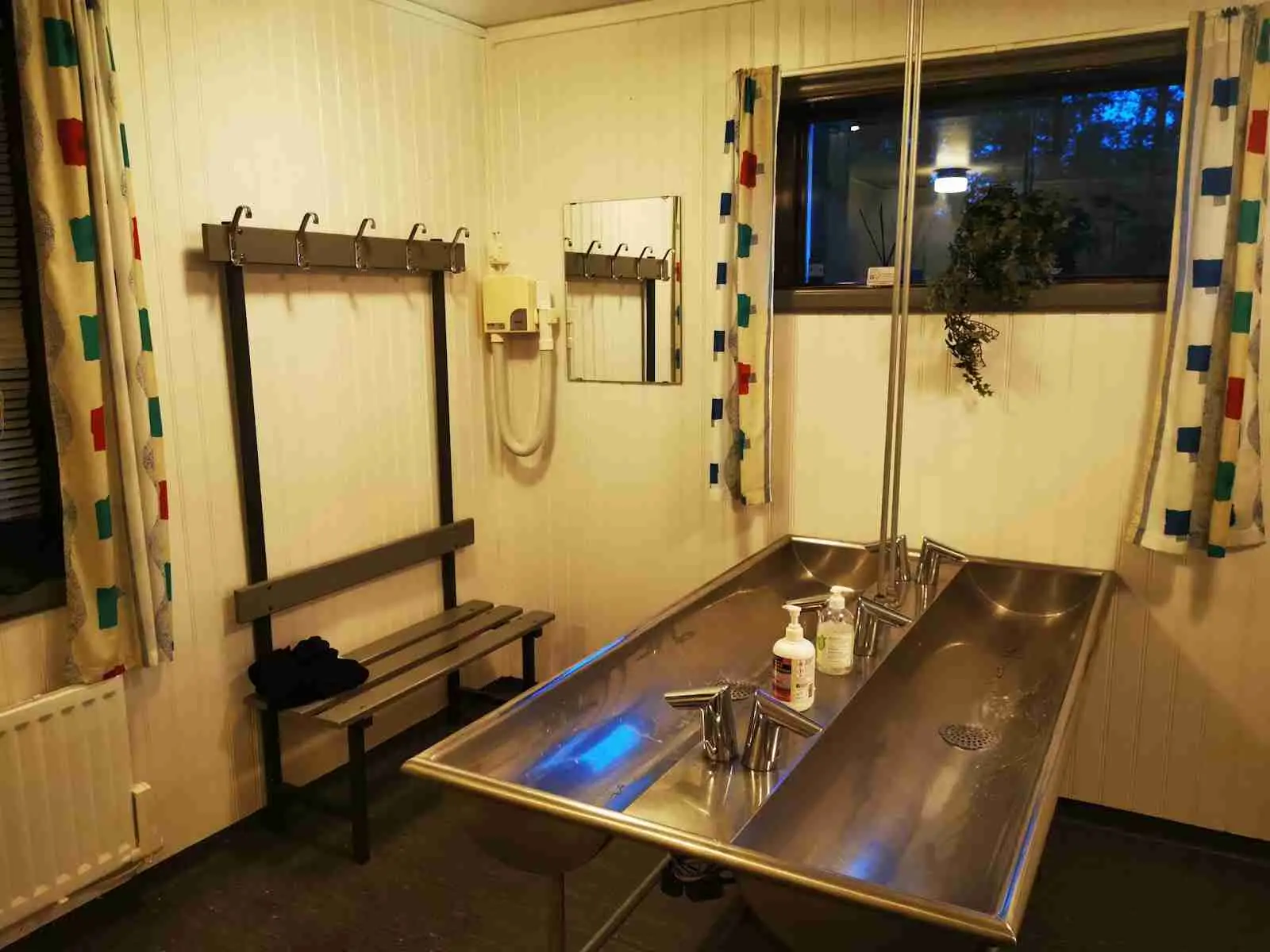 En modern campingstuga med trägolv och stilren inredning. Rummet har god belysning med moderna lampor i taket. Glasskiva som avskiljare och ett glänsande modernt vattenkran tillsammans med snygg träfinish på möblerna skapar en inbjudande atmosfär.