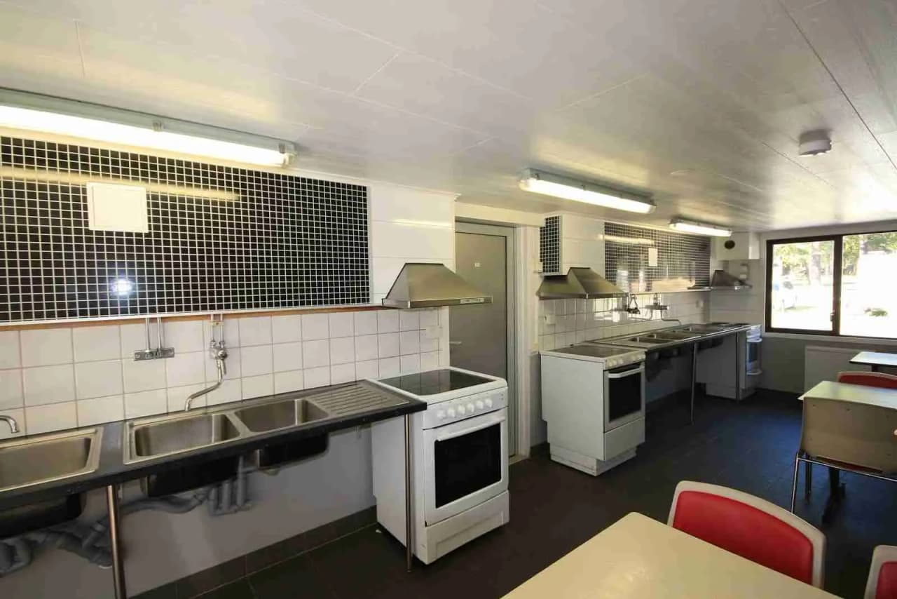 Alt-text: Modernt kök på Rösjöbaden Camping & Stugby med ljust innertak, stilren bänkskiva, mörkt golv och eleganta köksapparater.