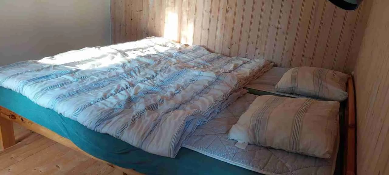 Ett sovrum på Löckna camping med en bekväm säng, trämöbler och träbaserat golv. Sängen är bäddad med enkla sängkläder och skapar en hemtrevlig atmosfär.