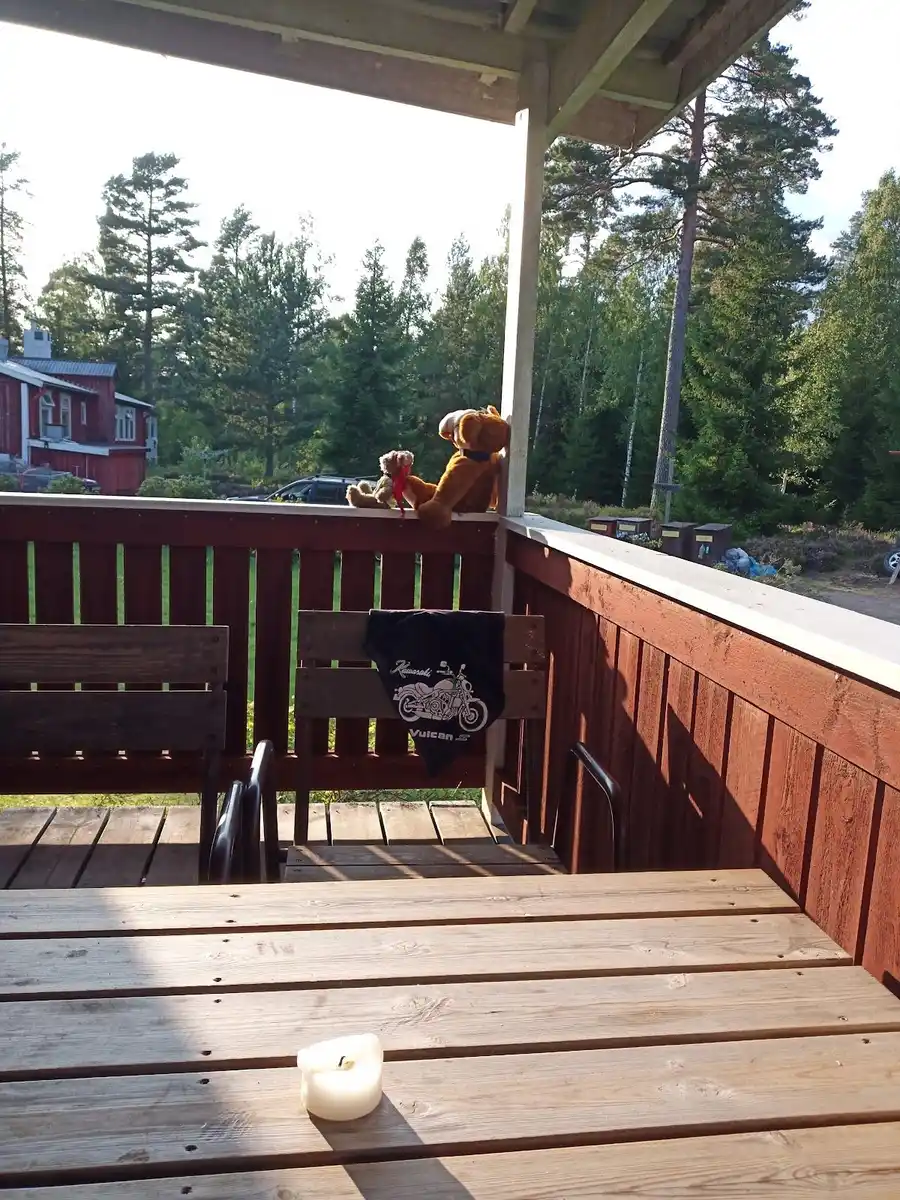 Alt-text: En träterrass vid Stigmansgården i Tiveden, med träplankor i olika nyanser och några utomhusmöbler som ger en inbjudande plats för vila och avkoppling i naturskön miljö.