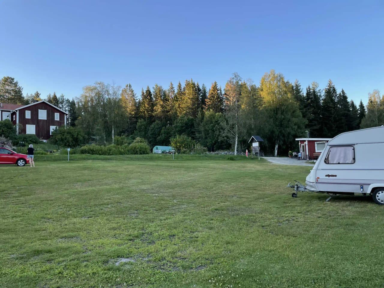 En grönskande campingplats med träd, gräs och parkerade husvagnar på Storsjö Camping & Trädgård.