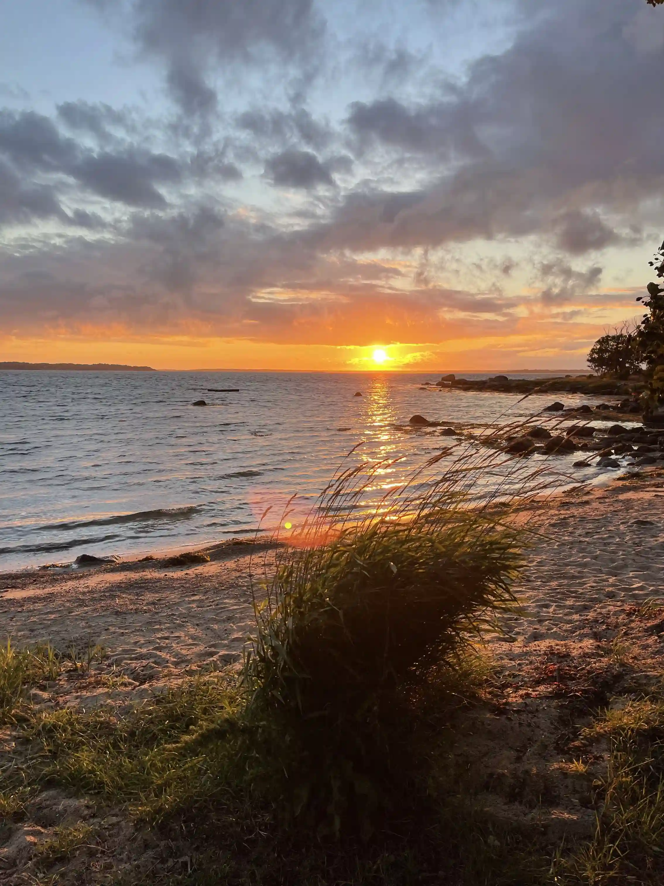En vacker vy vid Stenbräckagården Hägnan med en horisont över vattnet under en solnedgång. Moln pryder himlen och stranden ligger vid kustkanten i skymningsljus.