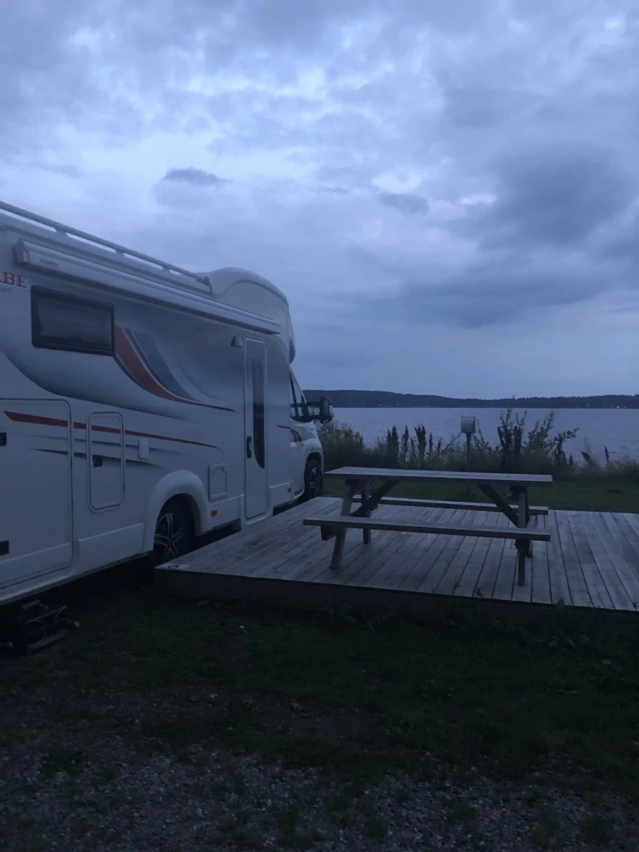 En husvagn vid Arvika småbåtshamn under solnedgången, med en färgglad himmel i bakgrunden som skapar en lugn och fridfull atmosfär.
