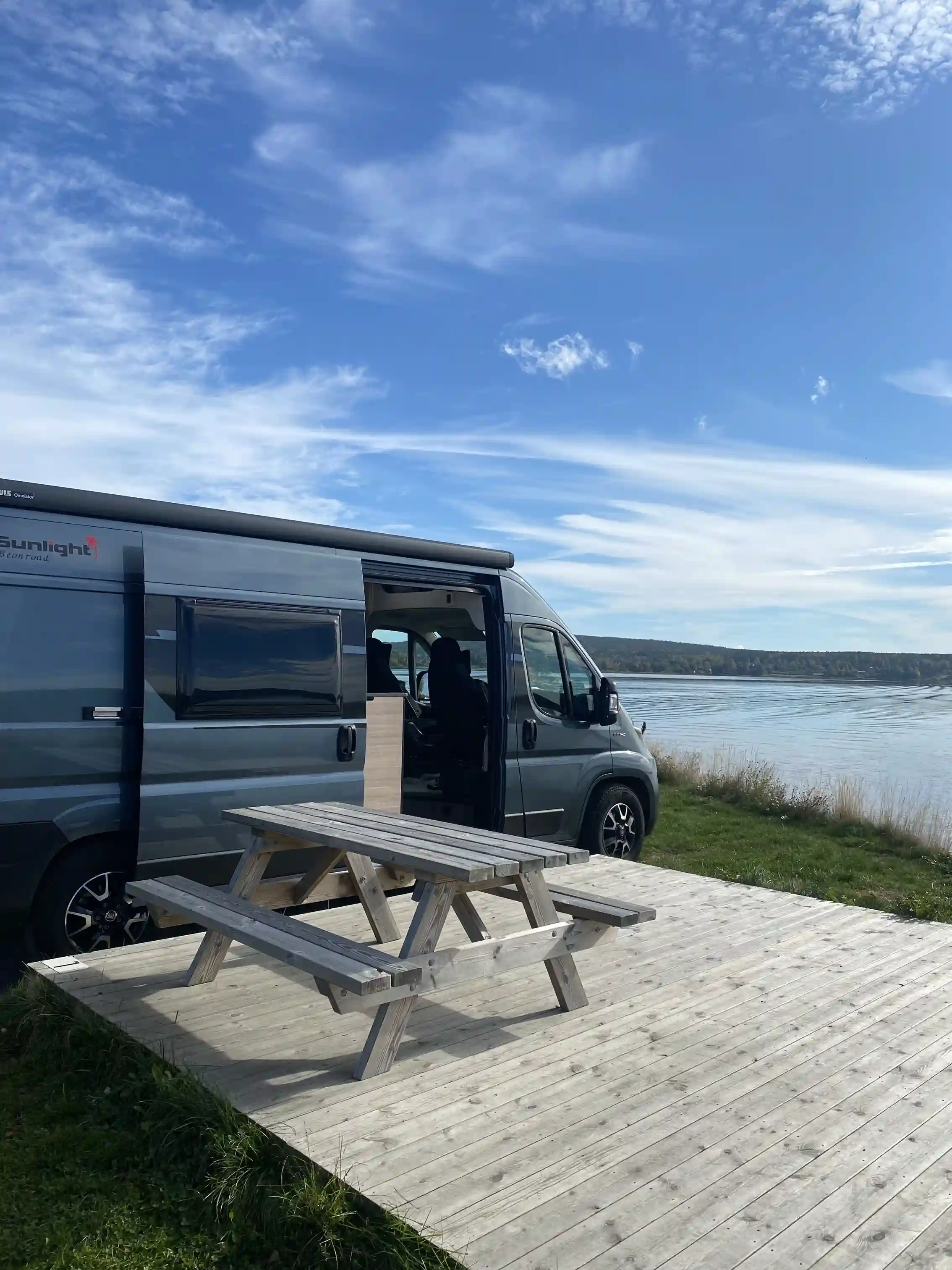 Alt-text: En småbåtshamn i Arvika med flera parkerade fordon, inklusive husbilar och minibussar, vid kajkanten, redo för sommarsäsongens besökare.