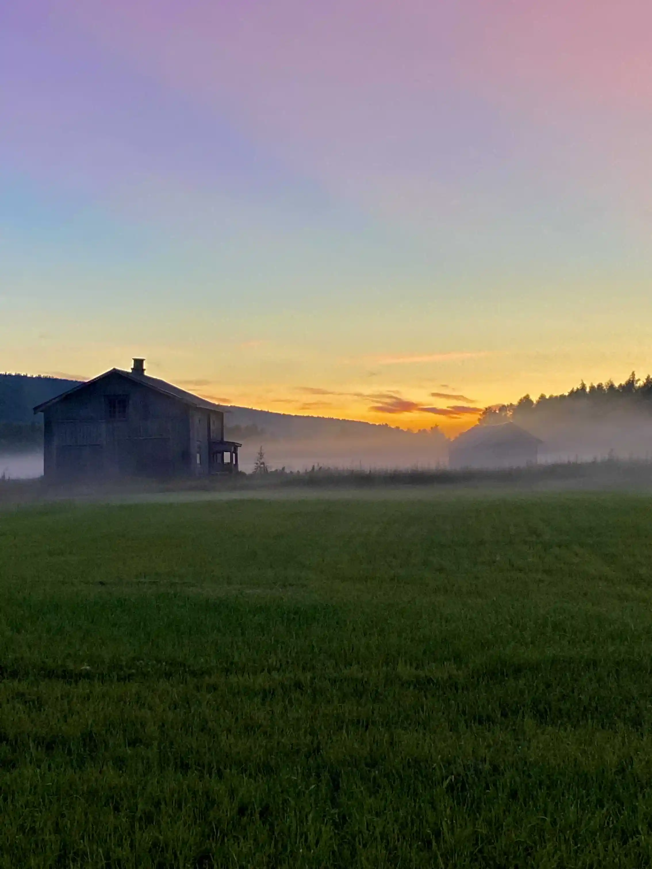 En vidsträckt äng omgiven av låga kullar vid solnedgång, himlen skiftar i varma toner.