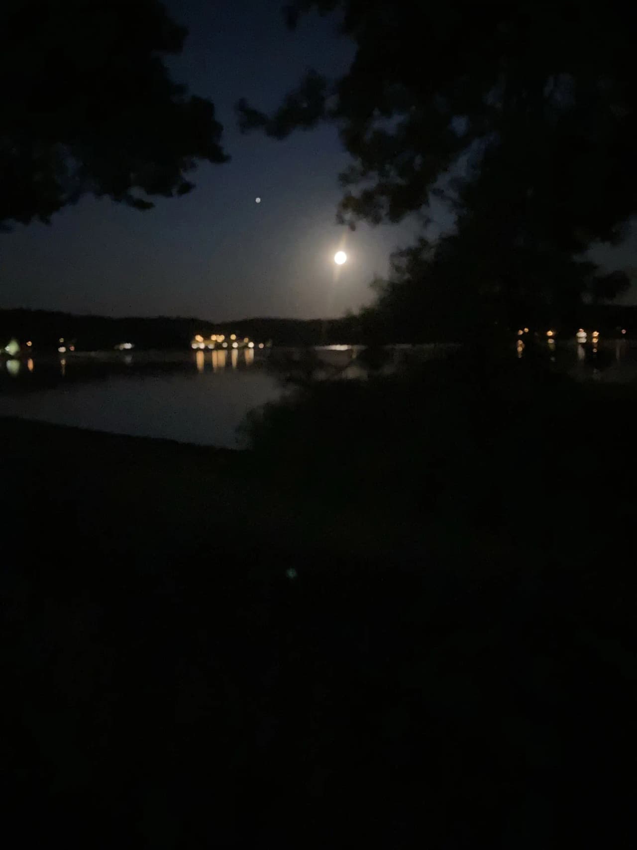 En stilla sjö på natten med månen lysande klart på himlen, vars ljus reflekteras på vattnets yta vid Hanatorps camping.