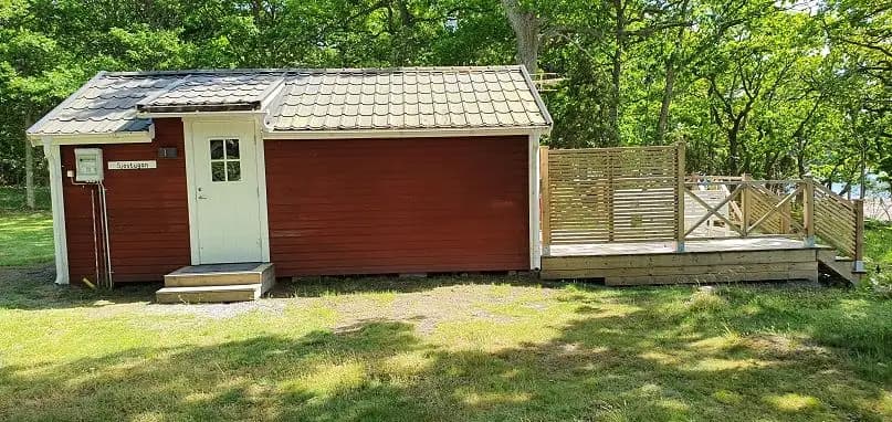 En bild av Kustgården Senoren visar en trästuga med ett sadeltak, belägen i en lantlig miljö. Omgivningen består av gröna trädgårdsbyggnader och en rymlig bakgård.