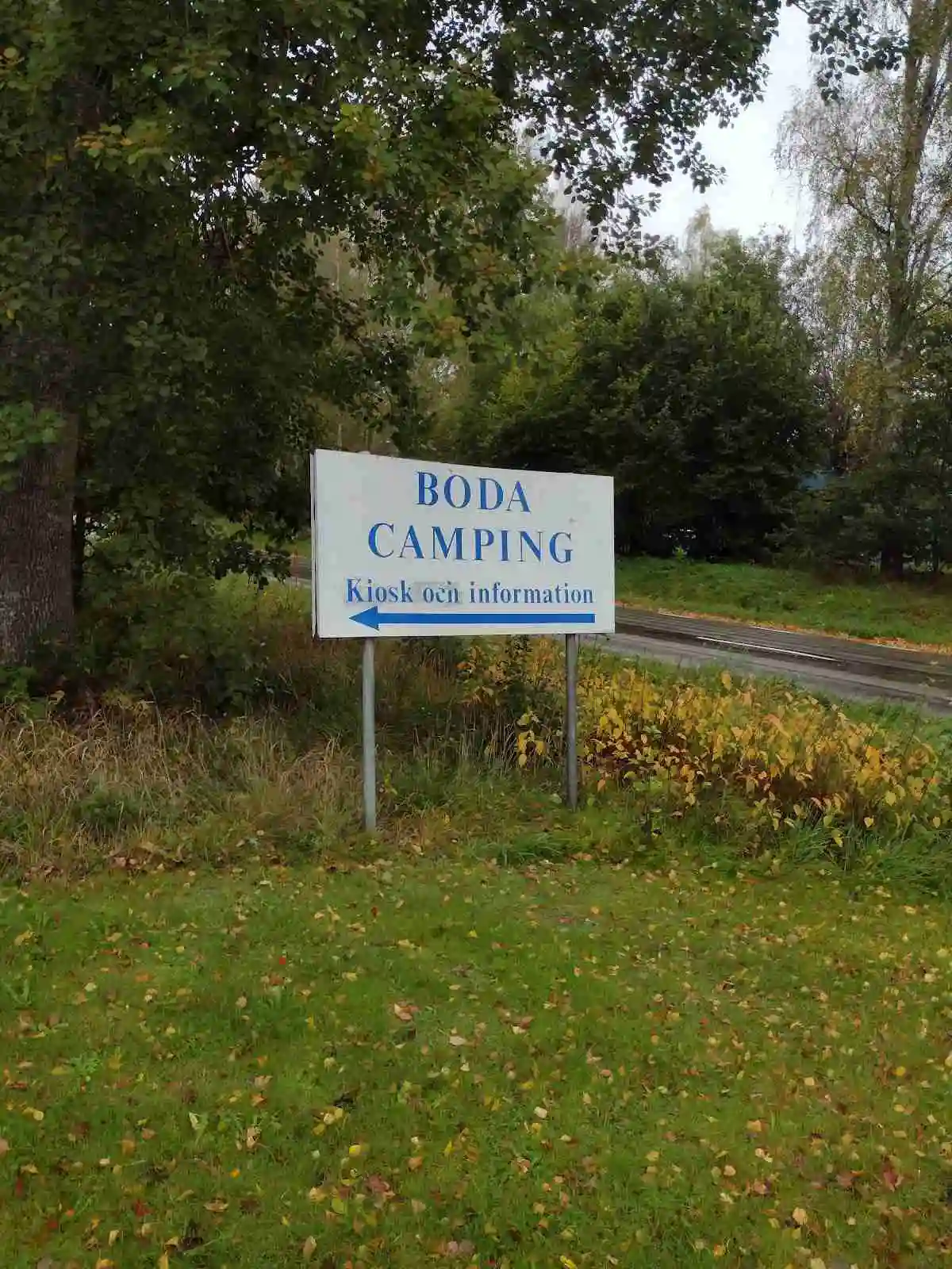 En grön campingplats i Emmaboda med tält och tarpar uppställda på en gräsmatta, omgiven av träd.