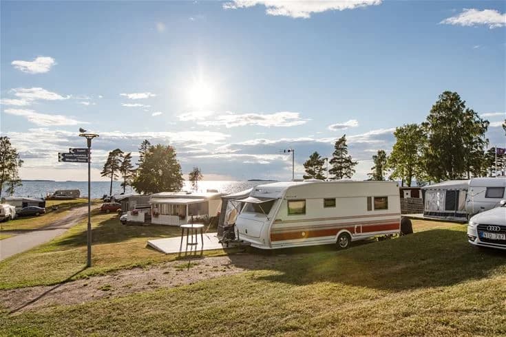 En husvagn parkerad på en grön campingplats omgiven av träd vid Askeviks Camping & Stugor.