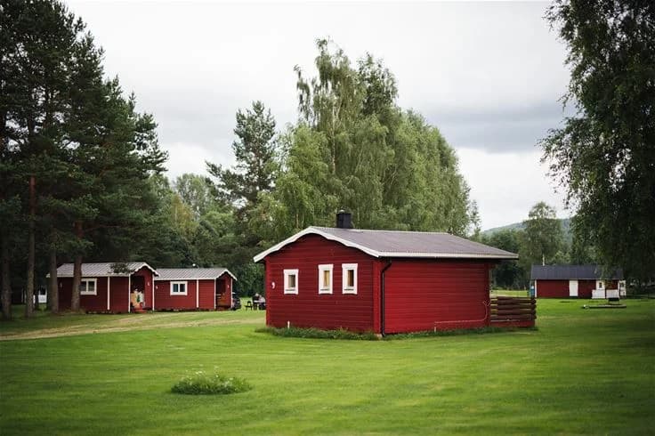 En grönskande campingplats vid namn Björkebo med gräsfält, träd och små stugor.