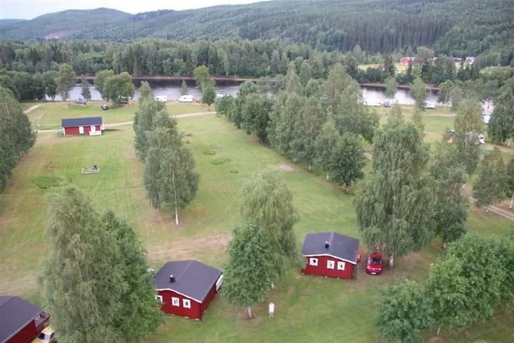 En lantlig och grönskande campingplats med gräsytor, träd och en stuga, belägen i en naturskön miljö.