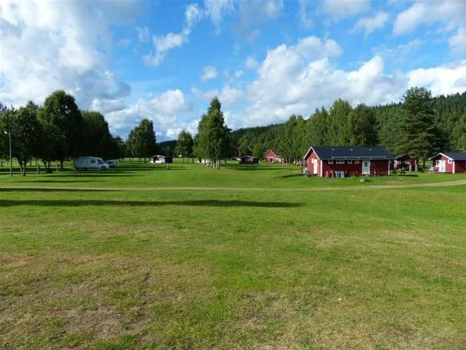 En vidsträckt grön äng under en molnig himmel, sannolikt en del av Björkebo camping, med frodig gräsmatta och omgivande natur.