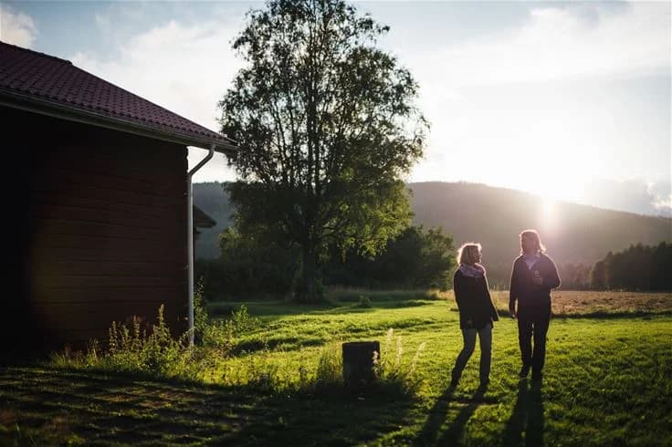 En grönskande campingplats med öppna gräsytor under sommarhalvåret. Området är omgivet av natur och landskapets mjuka kullar, där människor kan ses njuta av solskenet under en klar morgon.