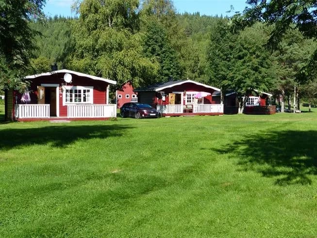 Bild av Björkebo Camping som visar en grön gräsmatta omgiven av träd. I bakgrunden syns stugor och en välskött gård, vilket bidrar till den naturnära och avkopplande atmosfären på platsen.