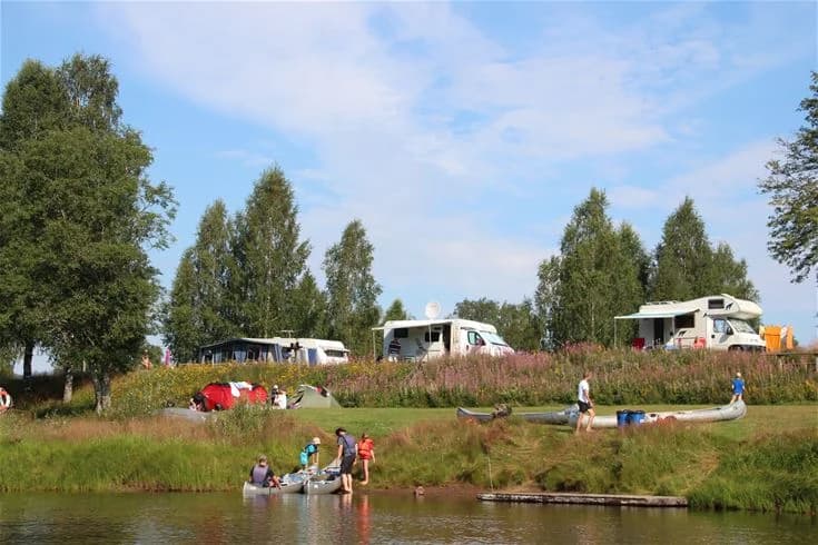 En liten båt ligger dockad vid strandkanten vid en naturskön flod eller sjö vid Björkebo camping, omgiven av frodig vegetation och med lugnt vatten som skapar en avkopplande miljö för rekreation och fritidsaktiviteter.