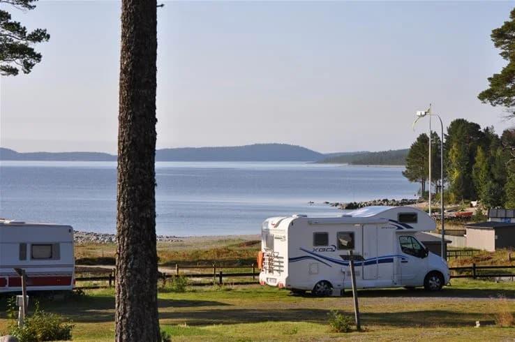 En husvagn står parkerad nära en strand vid havet på Gullviks Havsbad Camping & Stugby. I bakgrunden syns havets blånande vidder och en sandig strandlinje som inbjuder till avkoppling och aktiviteter.