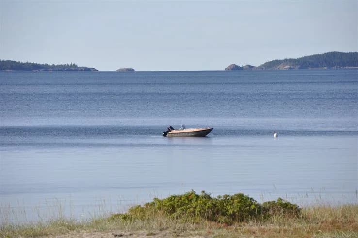 En vy över en kustnära campingplats med båtar till sjöss, vid Gullviks Havsbad Camping & Stugby. Rent, blått hav omger småbåtar vid en lugn strandlinje i naturskön miljö.