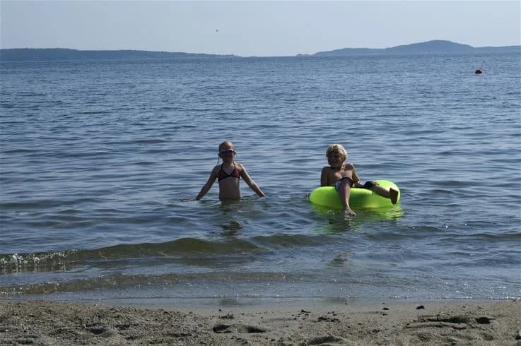 En somrig strand vid Gullviks Havsbad Camping & Stugby, med folk som njuter av sol och bad vid havet.