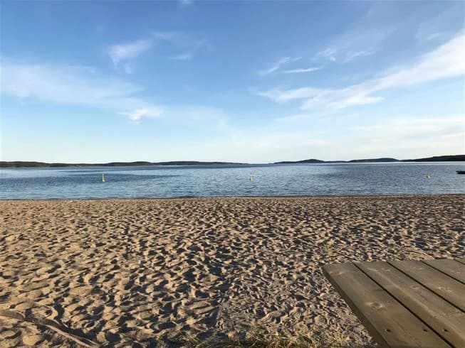 En somrig bild av Gullviks havsbad camping & stugby med en vidsträckt blå horisont där vattnet möter himlen. Förgrunden visar en solbelyst sandstrand vid kusten.