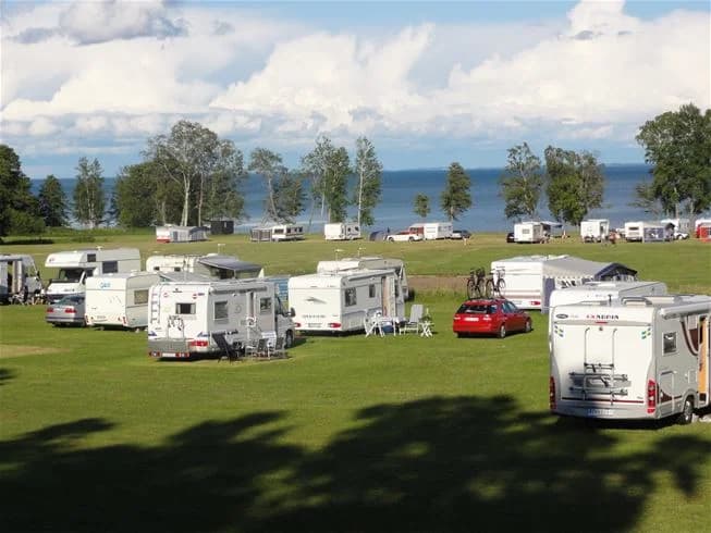 En grön campingplats på Breviks camping & ställplats med husvagnar, tält och vidsträckta gräsmattor under en klar himmel.