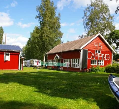 En grön gräsmatta med ett picknickbord under skugga framför en stuga vid camping 45.