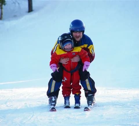 En grupp skidåkare har roligt i snön på Camping 45, iförda vinterkläder och hjälm för säkerhet medan de njuter av en vinterdag i det glittrande landskapet.