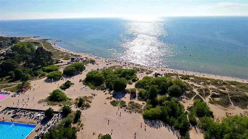 En strand vid Tofta Camping, med människor som njuter av sommaren vid havet. Flygfoto visar kusten och det öppna havet i bakgrunden.